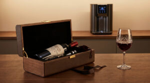 Coffret cadeau en bois contenant une bouteille de vin, un tire-bouchon, un bouchon et un verre à vin sur une table.