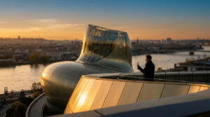 Man holding a glass of wine on the rooftop terrace of the golden, uniquely shaped La Cité du Vin museum in Bordeaux.